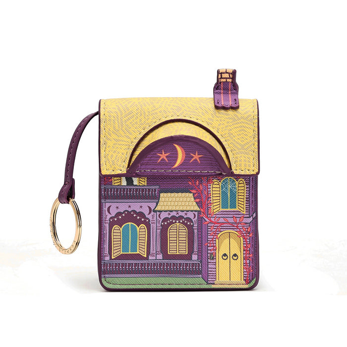 A small zip-around wallet with a wrist strap, featuring a colorful illustration of a house facade on the front. The wallet has a textured yellow top flap, a purple arched section with a crescent moon and stars, and a lower section with purple, yellow, green, and red architectural details.