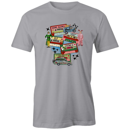A dark gray graphic print featuring Christmas-themed cassette tapes and characters from The Grinch movie, including a green and yellow Elf, a pink Grinch in a onesie, and a green station wagon with a Christmas tree. Text includes 'Home Alone', 'Elf', 'Grinch', and 'National Lampoons Christmas'.