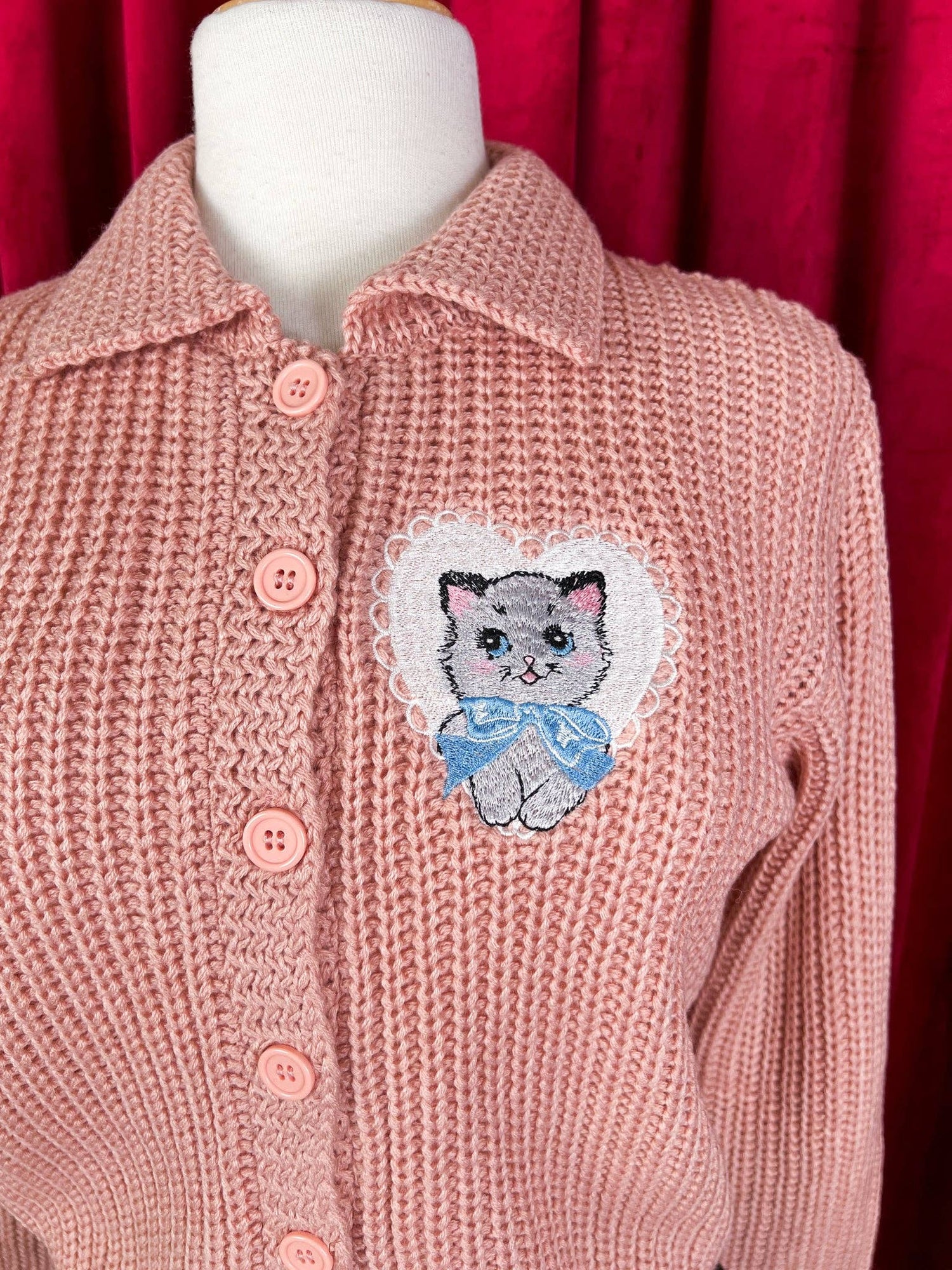 Pink knitted cardigan with a embroidered cat patch on a red background