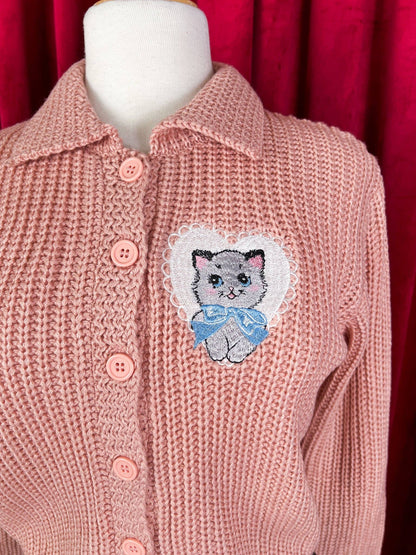 Pink knitted cardigan with a embroidered cat patch on a red background