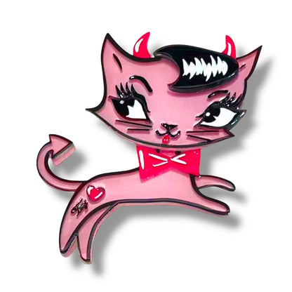 A pink cartoon cat charm or pin with devil horns, a black hairpiece, white fangs, a red bow tie, and a small red heart on its back, shown on a white background with a drop shadow.