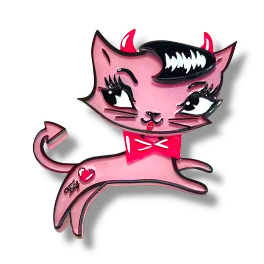 A pink cartoon cat charm or pin with devil horns, a black hairpiece, white fangs, a red bow tie, and a small red heart on its back, shown on a white background with a drop shadow.