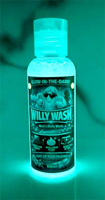 A bottle of glow-in-the-dark body wash labeled 'Willy Wash' glowing bright cyan under dark conditions, set against a dark green background.