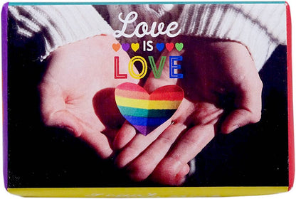 A square greeting card or print featuring a close-up of two hands holding a rainbow-striped heart, with the words 'Love IS LOVE' printed above. The card has a colorful border and is photographed against a dark background.