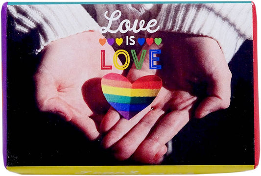 A square greeting card or print featuring a close-up of two hands holding a rainbow-striped heart, with the words 'Love IS LOVE' printed above. The card has a colorful border and is photographed against a dark background.