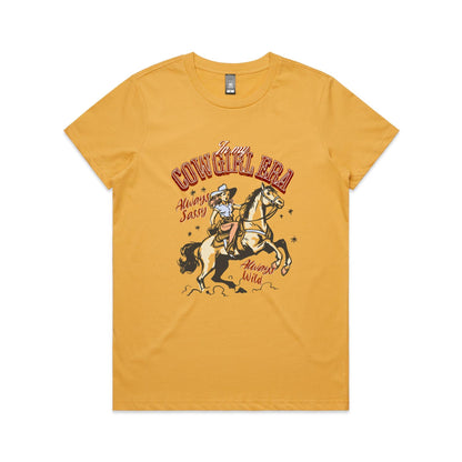 A white graphic t-shirt featuring a retro western illustration of a cowgirl riding a horse. The text reads 'In my COWGIRL ERA' in arched red letters, 'Always Sassy' in red script, and 'Always Wild' in red script, with the cowgirl wearing a cowboy hat and boots while riding a rearing horse.