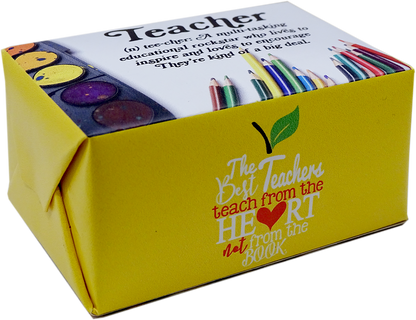 A yellow gift box for a Teacher-themed book, featuring colorful illustrations of colored pencils, paint palettes, and a green leaf. The front of the box displays the quote 'The Teachers teach from the HEART not from the BOOK' in stylized text.