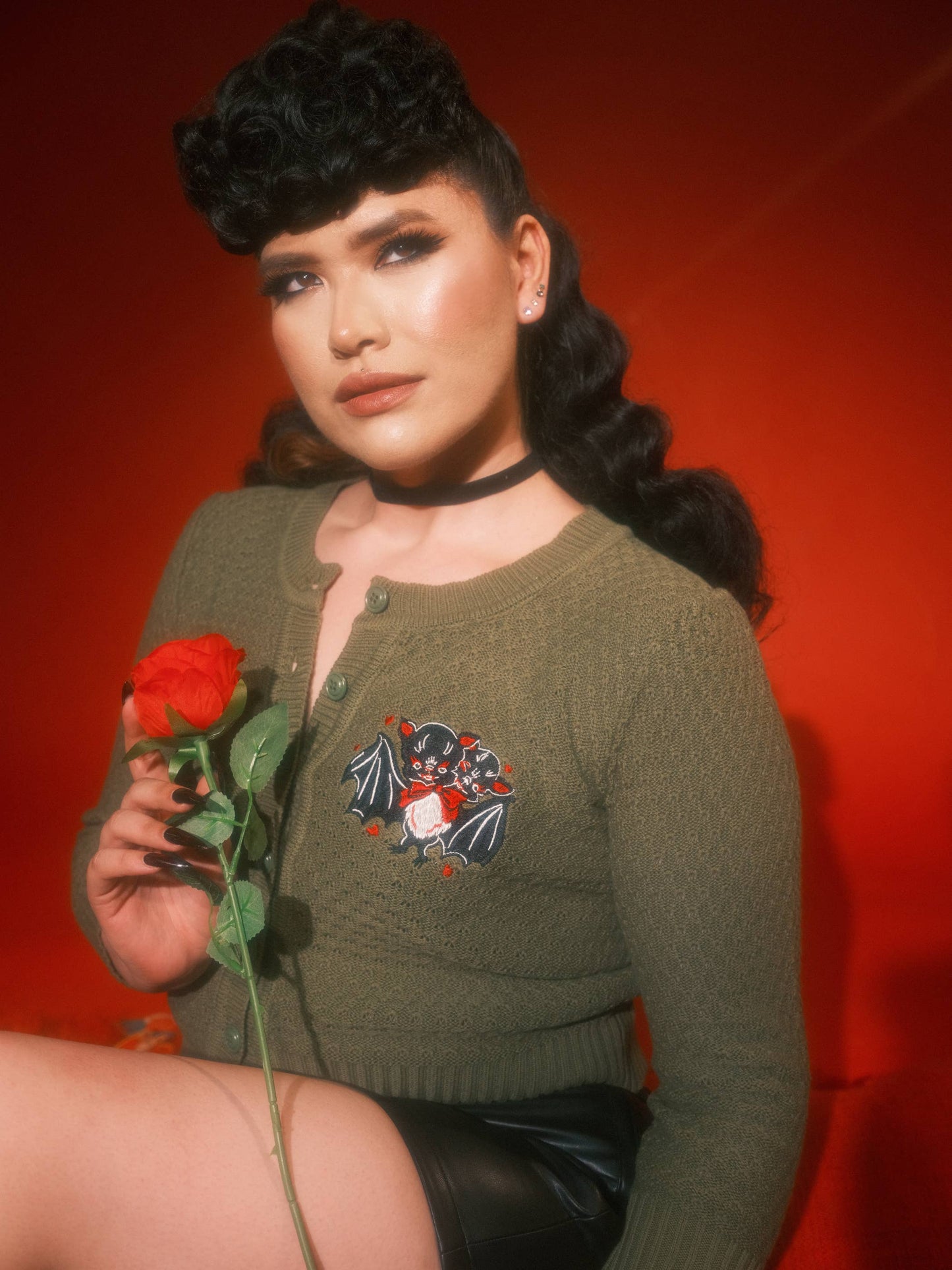 Woman holding a red rose wearing a green sweater with a floral design against a red background