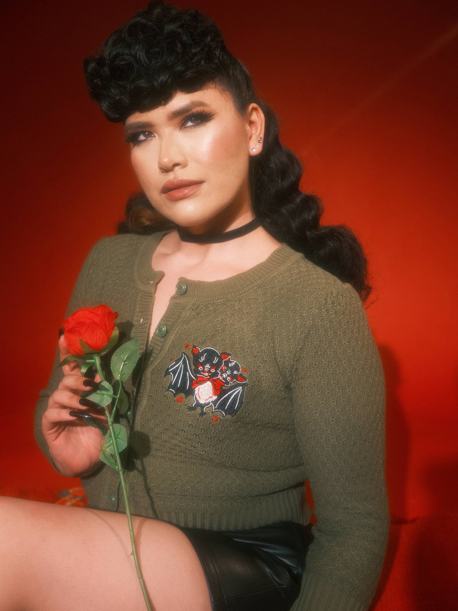Woman holding a red rose wearing a green sweater with a floral design against a red background