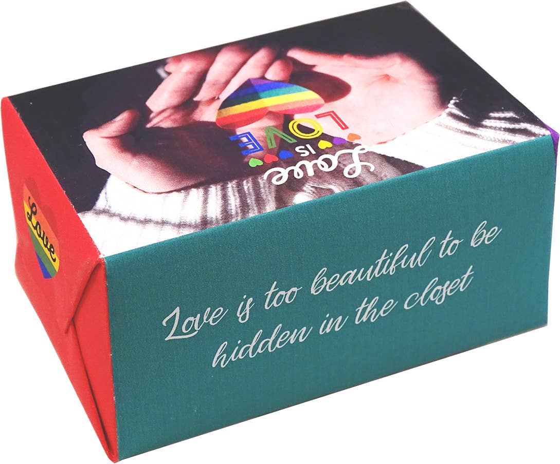 A rectangular gift box with a teal front panel and red side panel, featuring printed artwork of hands holding a rainbow heart and the phrase 'Love is too beautiful to be hidden in the closet' in white script.