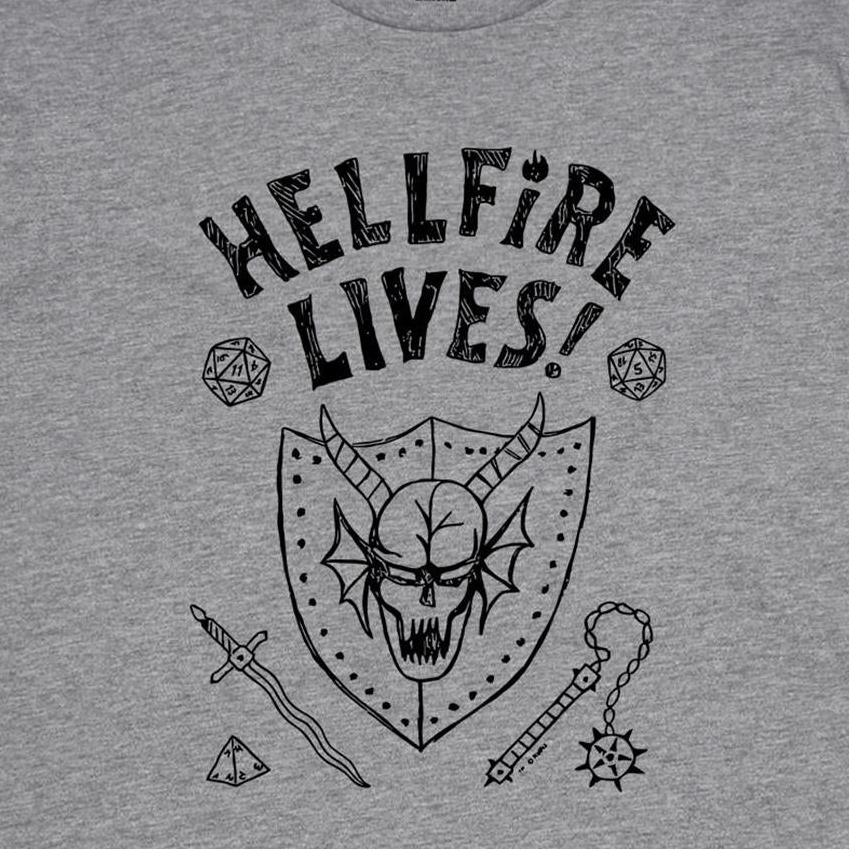 A close-up of a heather gray t-shirt featuring a black graphic print with the text 'HELLFIRE LIVES!' above a horned skull, dice, sword, and mace design.