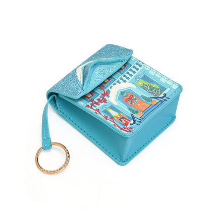 A small turquoise blue card holder wallet with a glittery flap and a colorful illustrated design on the front, featuring a matching key ring.