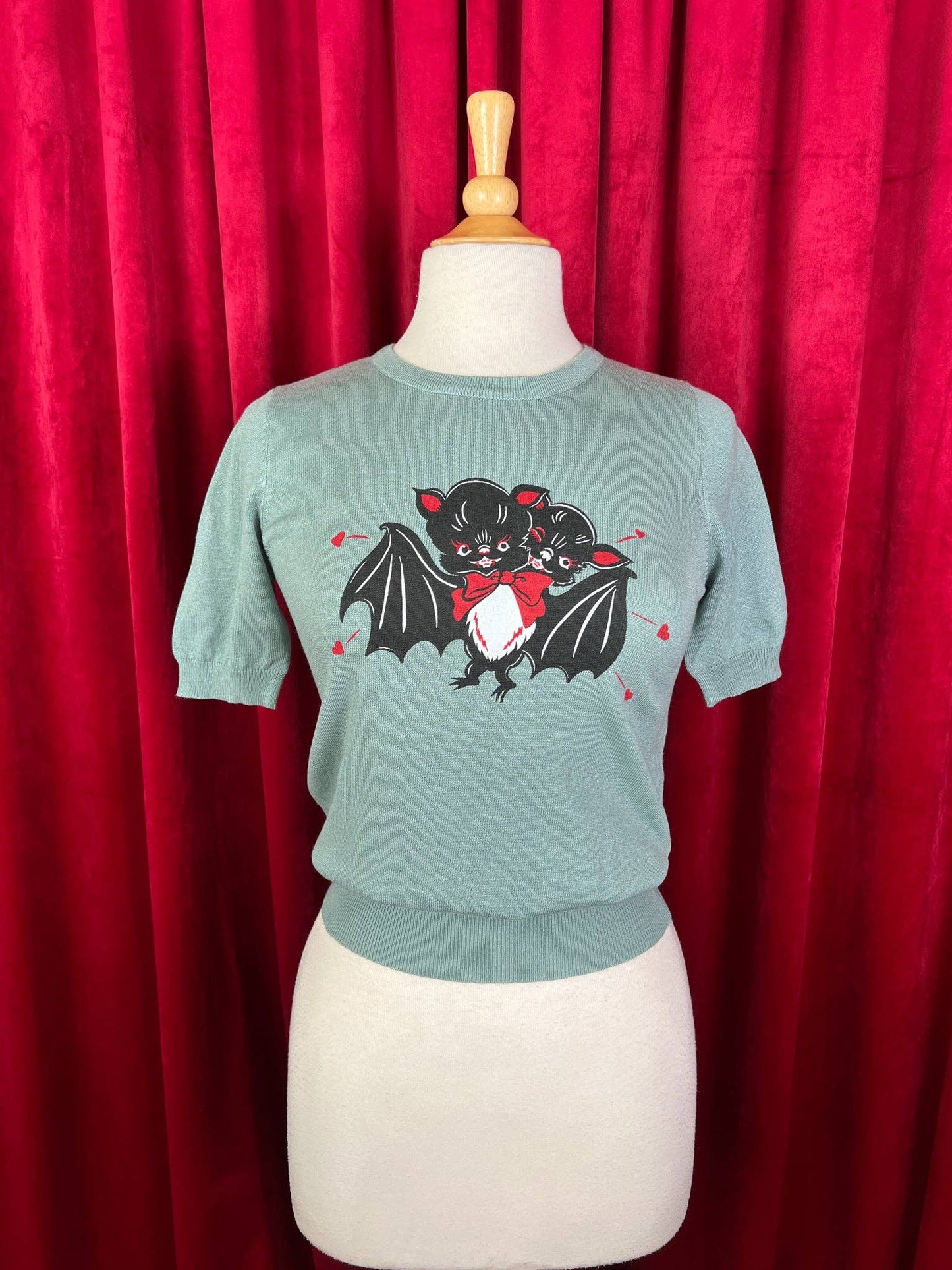 Teal sweater with bat design on a mannequin against a red curtain background