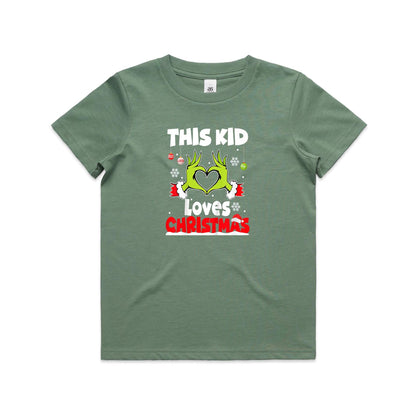 A close-up of a green Christmas t-shirt featuring a graphic of the Grinch's hands forming a heart, with the text 'THIS KID Loves CHRISTMAS' in white and red.