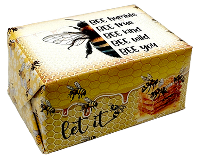 A square gift box wrapped in yellow honeycomb-patterned paper with illustrations of bees, honeycomb cells, and a honeycomb block. The top features a large bee graphic and the text 'BEE humble BEE true BEE kind BEE wild BEE you', and the bottom reads 'let it'.