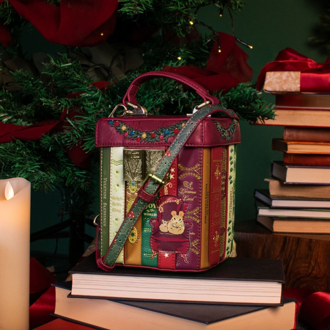 Decorative book-shaped handbag on books with a Christmas tree and candles in the background