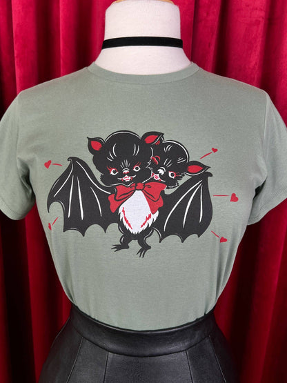 Green t-shirt with bat and cat graphic on a mannequin against a red curtain background