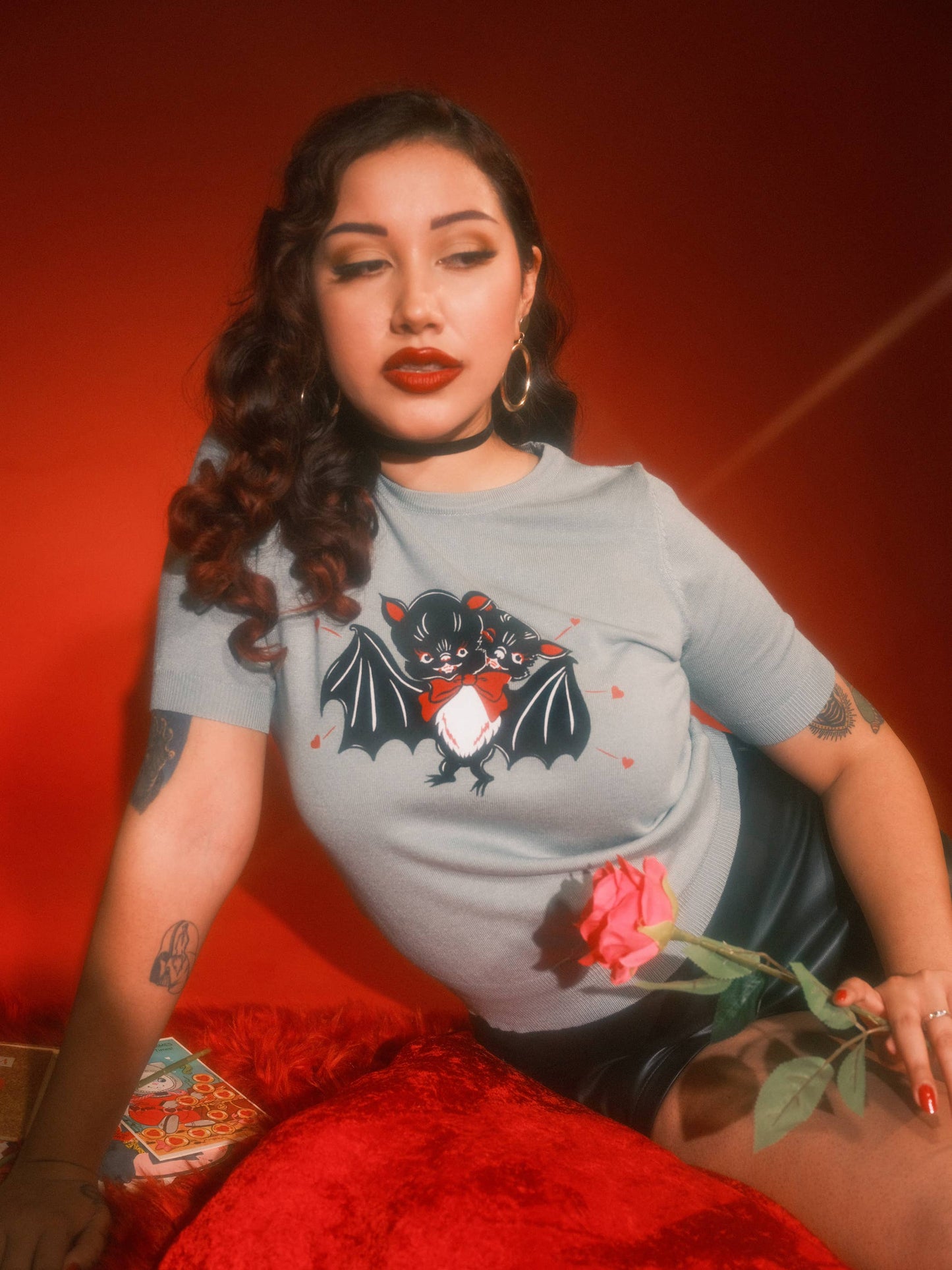 Woman wearing a t-shirt with a graphic design, sitting against a red background
