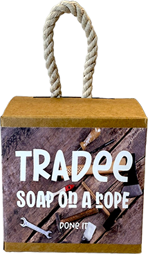 A square cardboard soap gift box with a thick rope handle, featuring a printed front panel that reads 'TRADEE SOAP ON A LOPE' and 'DONE IT' over a rustic wood background.