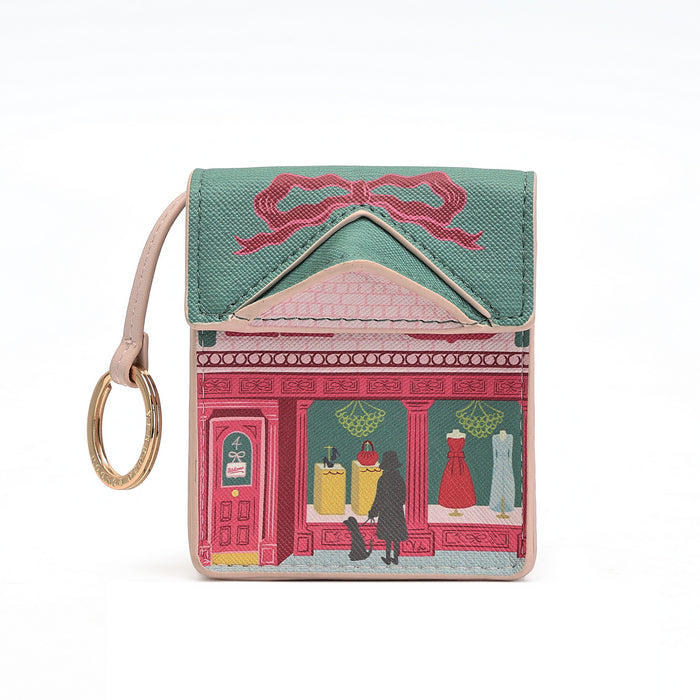 A small leather card holder or wallet featuring an embroidered pink storefront design with a teal top panel, pink bow embroidery, and a light pink wrist strap with a gold-tone ring, shown on a white background.