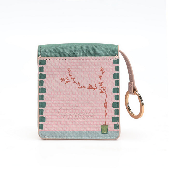 A small square card holder wallet by Vendimia London, featuring a pink patterned front with a botanical branch illustration, a teal top panel, a pale blue bottom border, and a tan wrist strap with a gold-tone ring on a white background.