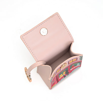 A small light pink faux leather card holder wallet with a snap button closure, shown open to reveal its interior. The exterior bottom edge features a colorful illustration of red double-decker buses, and it is accented with a small gold-tone ring clasp.