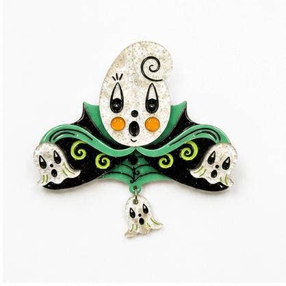 A Halloween-themed enamel pin featuring a stylized ghost face with black eyes and orange cheeks, a green collar with black and green swirls, and three small white skulls and a hanging ghost at the bottom, set against a plain white background.