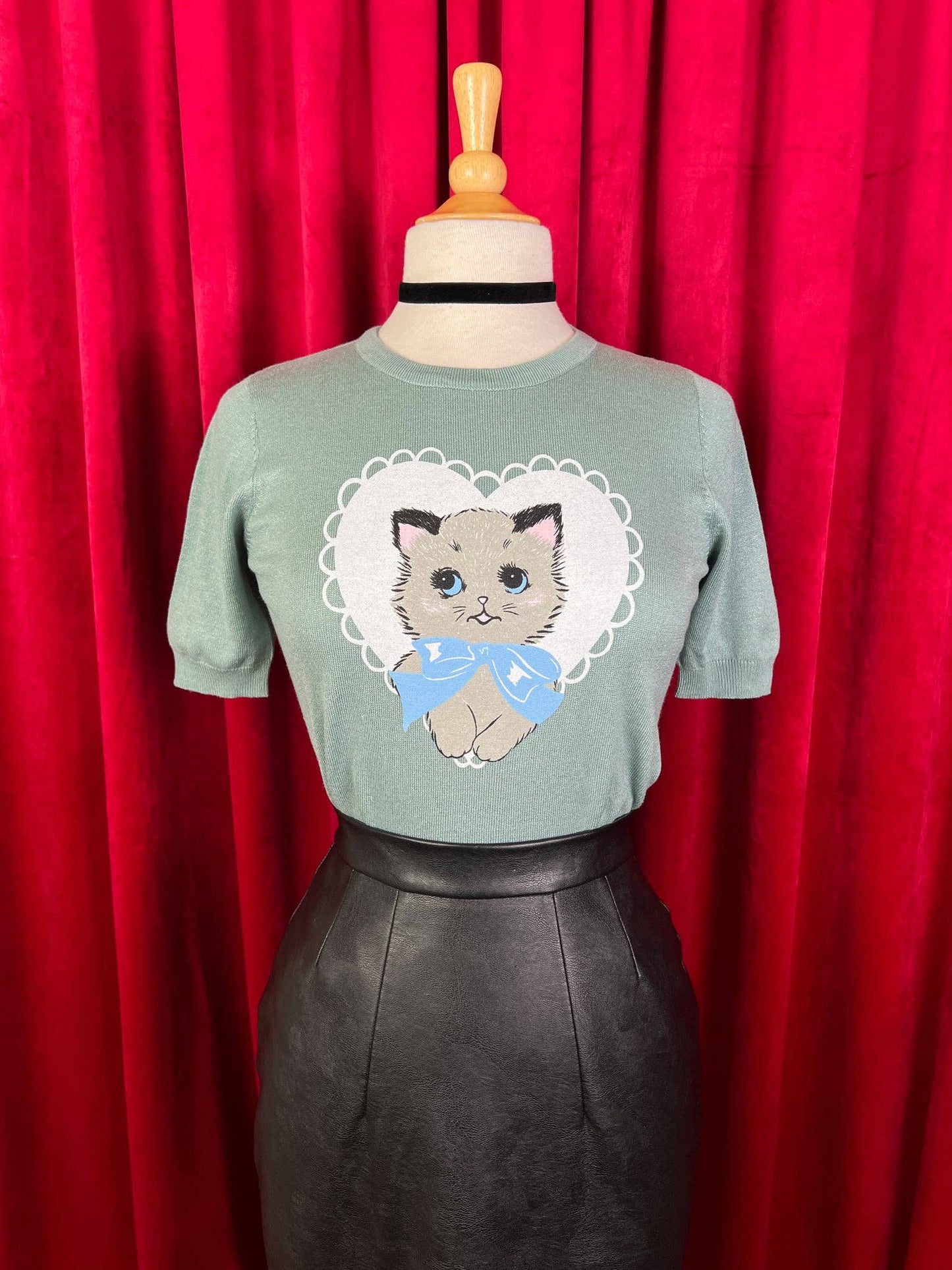 Green t-shirt with a cat graphic on a mannequin against a red curtain background