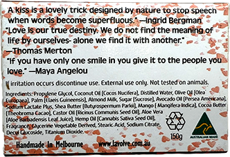 A square printed card or label with a white background, featuring a poem by Ingrid Bergman and Thomas Merton, plus May Angelou quote, along with ingredients, a small logo, and a recycling symbol. The card is decorated with a pink floral border and has a small green hand-drawn heart in the bottom right corner.