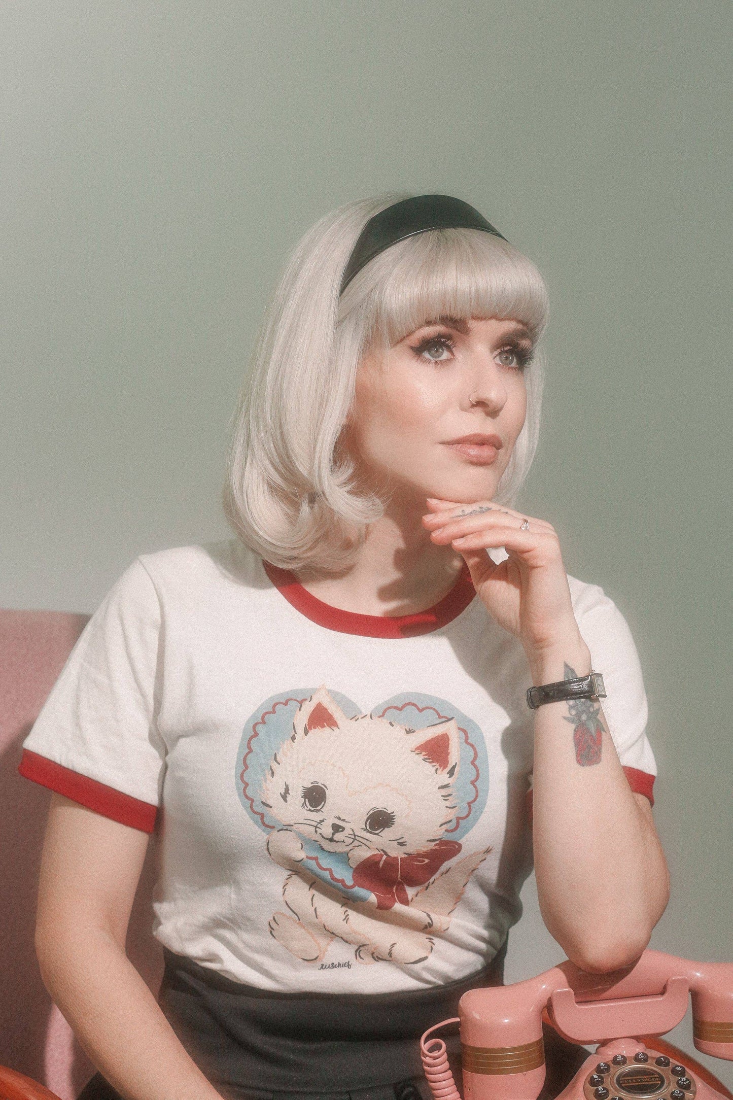 Person wearing a t-shirt with a cat graphic design, sitting against a plain background