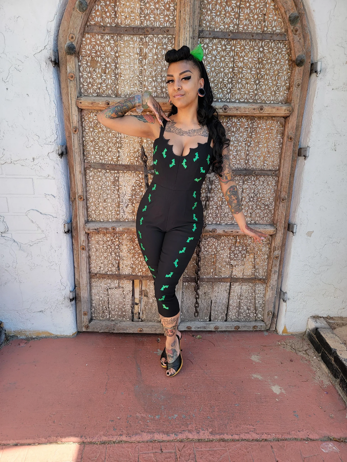 Woman in a black outfit with green patterns standing in front of an ornate wooden door.