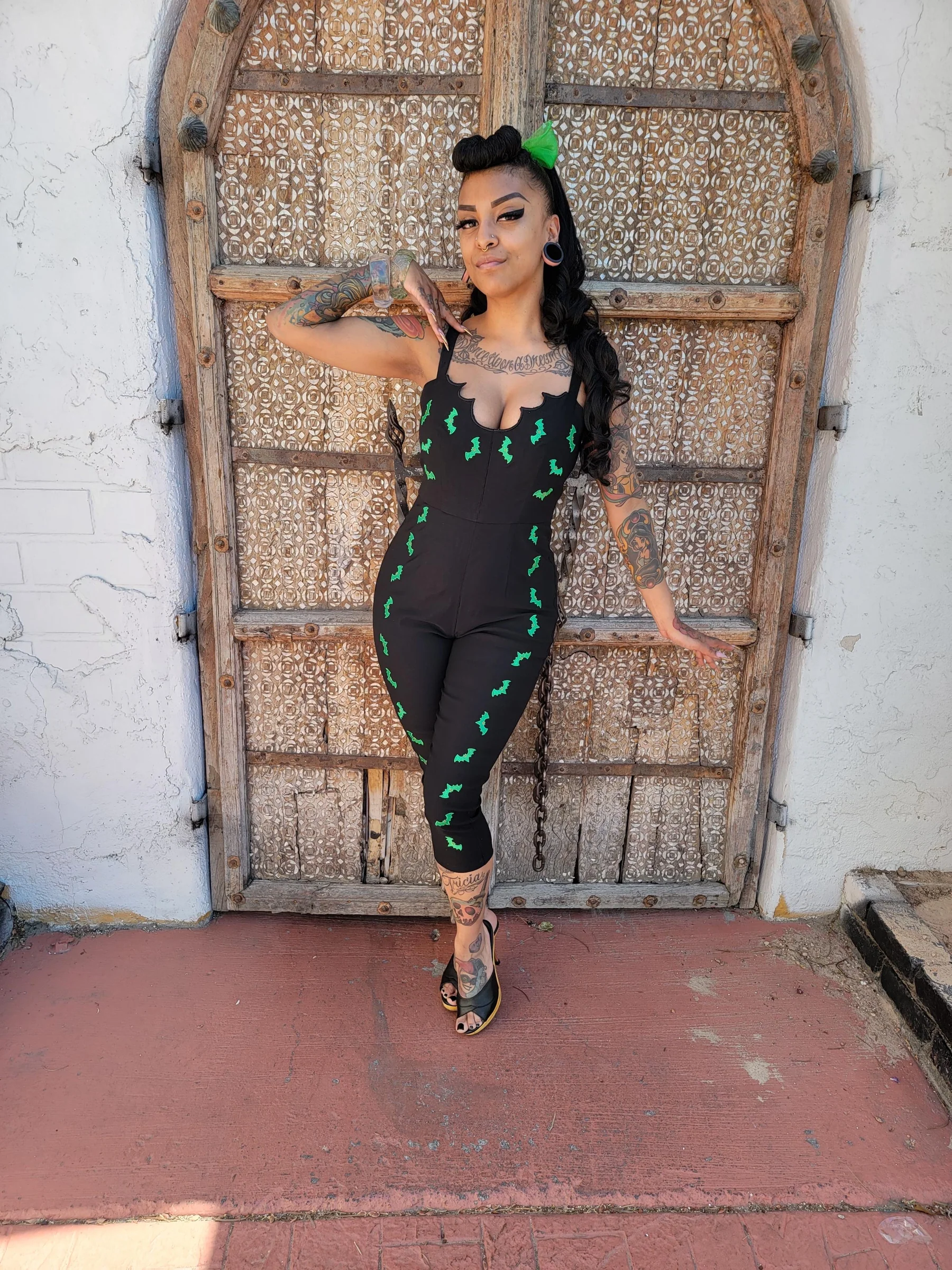 Woman in a black outfit with green patterns standing in front of an ornate wooden door.