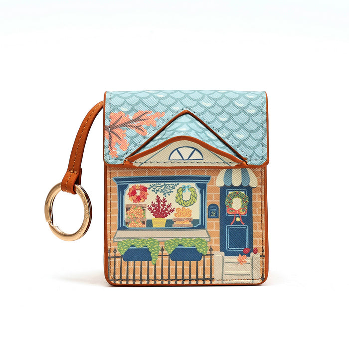 A small leather card holder or wallet featuring an embroidered storefront design with a blue patterned roof, brown trim, and a gold-tone key ring attached on a white background.