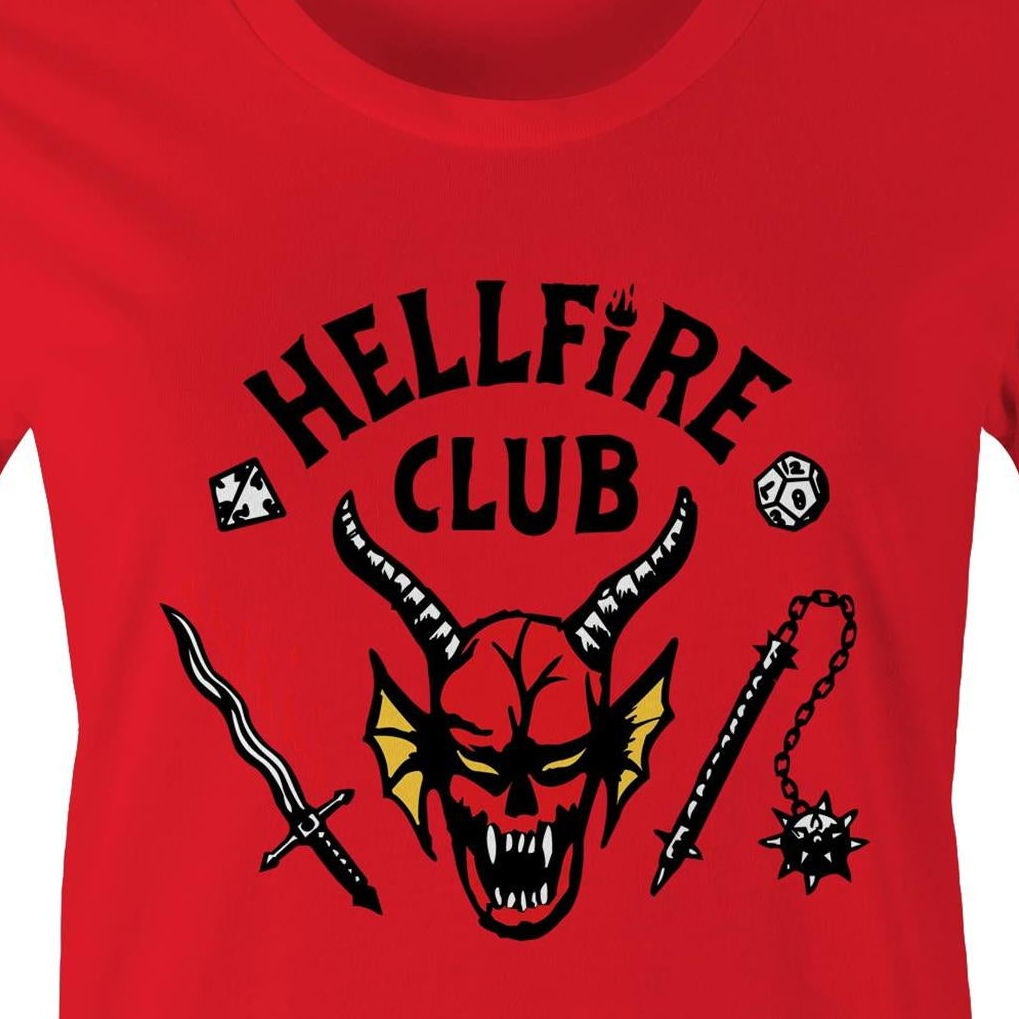 A close-up of a bright red t-shirt featuring a black graphic print that reads 'HELLFIRE CLUB' above a horned devil head with yellow wings, flanked by a sword and a spiked mace.