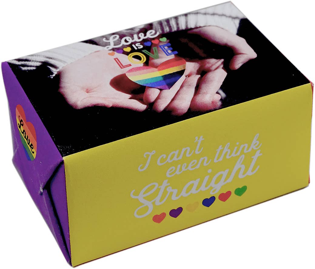 A rectangular gift box with a yellow front panel and purple side panel, printed with the phrase 'I can't even think Straight' in white script and small rainbow hearts. The top lid shows a photo of two hands holding a rainbow-striped heart, with the word 'Love' overlaid.