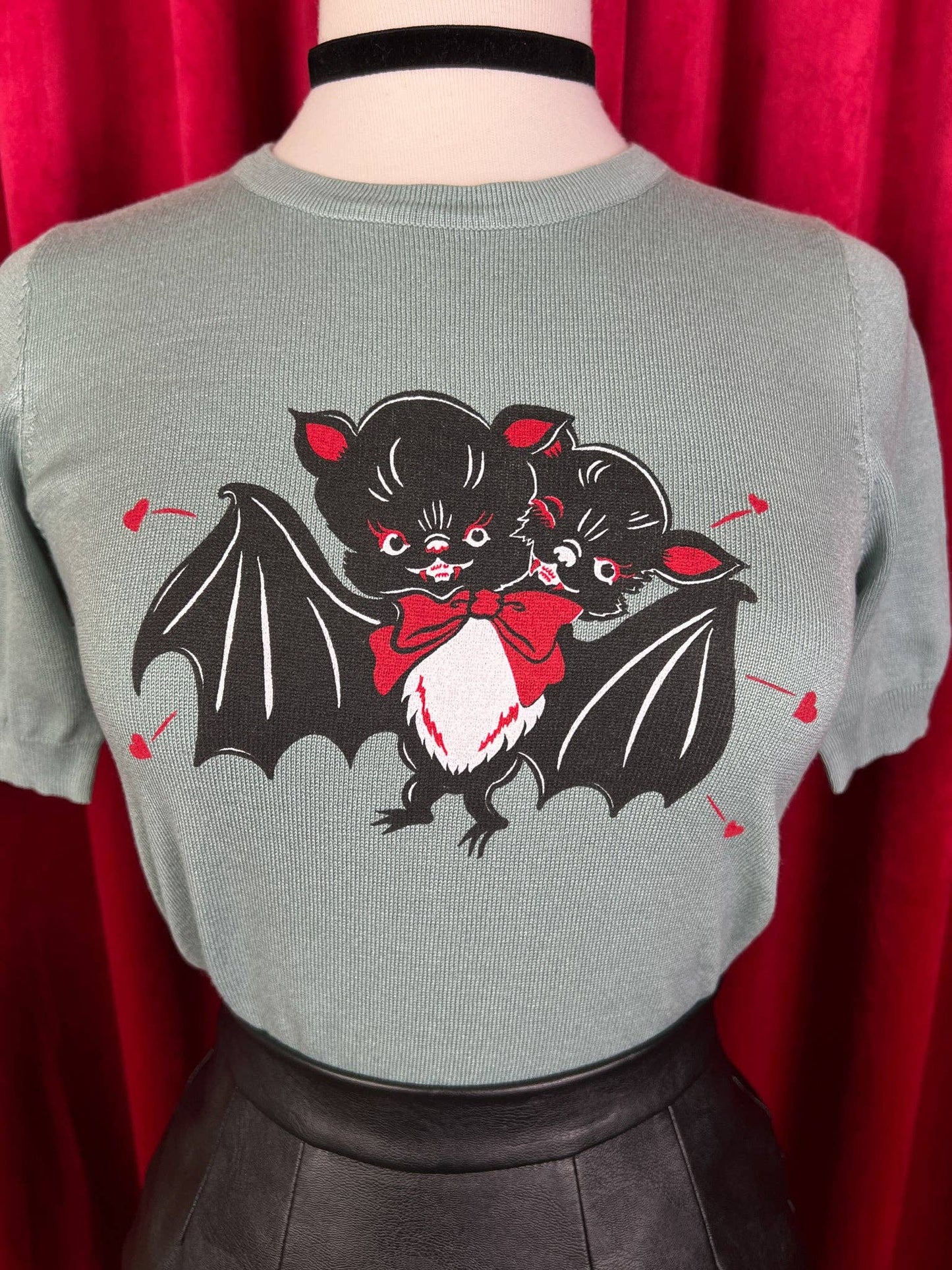 Gray sweater with black and red bat design on a red curtain background