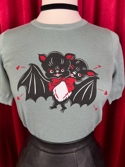 Gray sweater with black and red bat design on a red curtain background