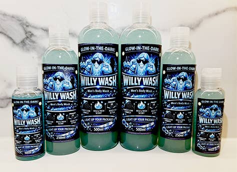 Six bottles of 'Willy Wash' men's body wash in various sizes arranged on a white marble surface. The bottles contain a translucent light blue-green liquid and feature black labels with blue and white graphics depicting a man in the shower, with the text 'GLOW-IN-THE-DARKS' and 'WILLY WASH'.