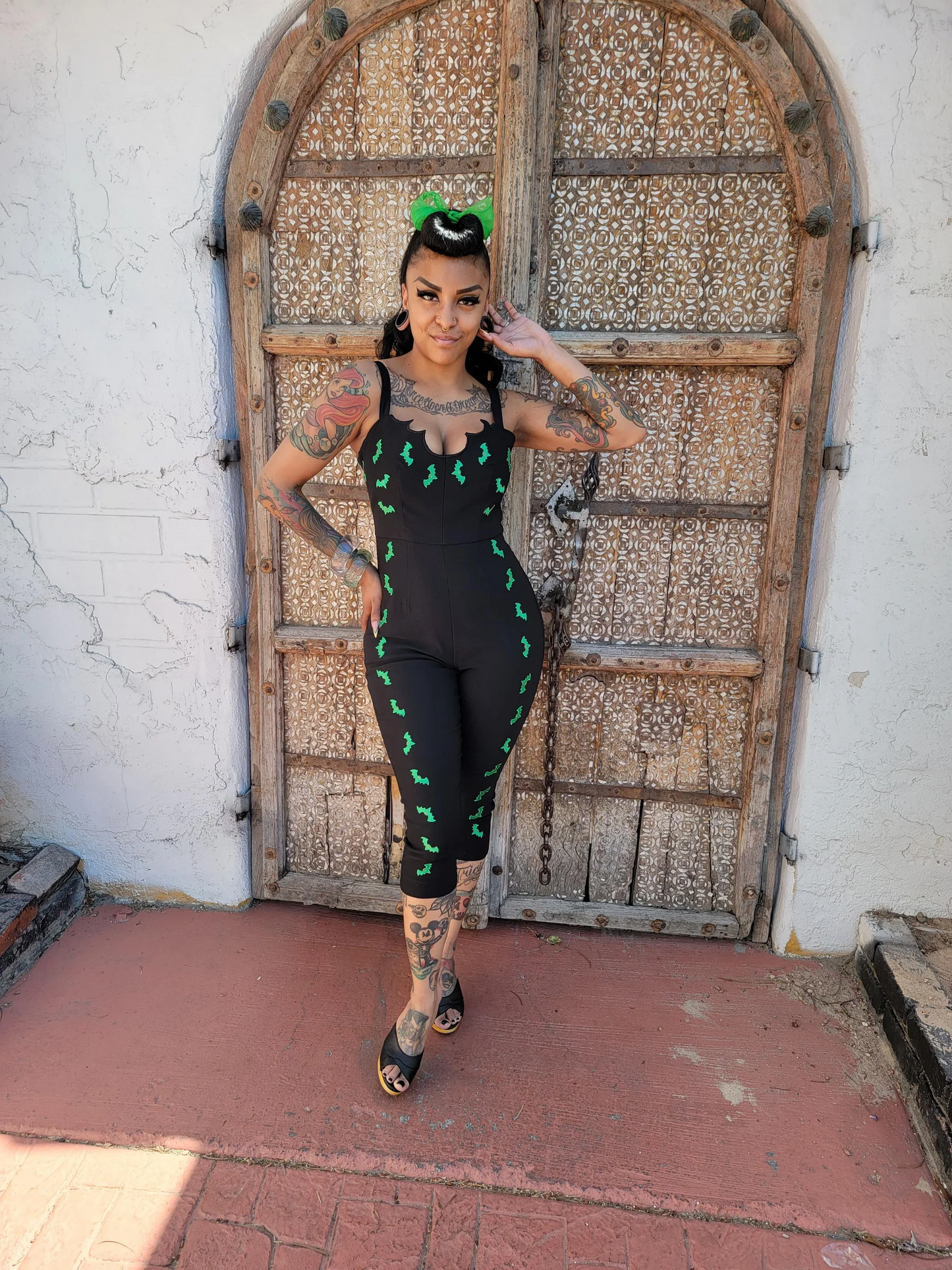 Person wearing a black outfit with green patterns in front of an ornate wooden door.