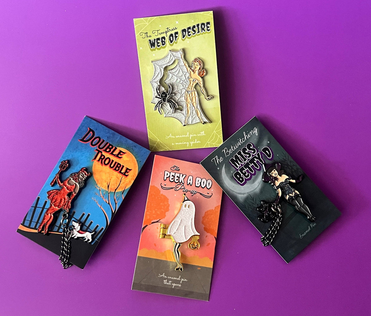 Three vintage-style enamel pin packages on a bright purple background. The packages feature retro illustrations and titles including 'The Temptation of Web of Desire', 'Double Trouble', 'The Peek a Boo Bag', and 'The Ransom of Miss Betty D'.