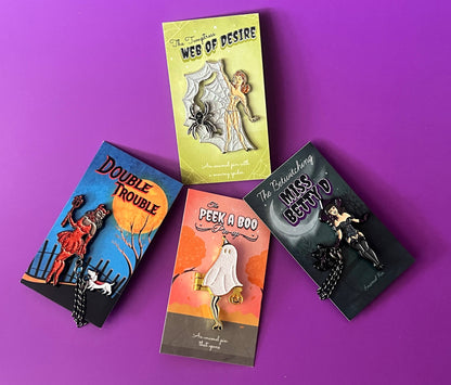 Three vintage-style enamel pin packages on a bright purple background. The packages feature retro illustrations and titles including 'The Temptation of Web of Desire', 'Double Trouble', 'The Peek a Boo Bag', and 'The Ransom of Miss Betty D'.