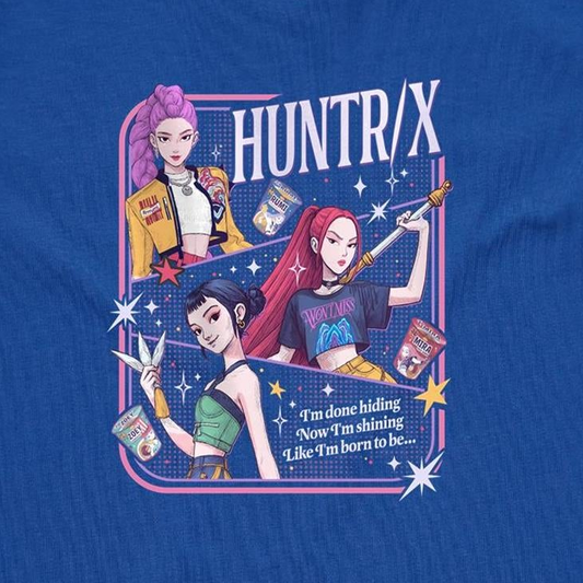 A close-up of a blue graphic t-shirt featuring three illustrated anime-style female characters with colorful hair and outfits, surrounded by stars and the text 'HUNTR/X'.