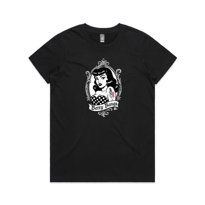 A black t-shirt featuring a vintage-style pin-up graphic of a woman with wavy black hair, a polka-dot top, and a tattoo reading 'BBB' on her arm, framed by an ornate silver border with a banner below reading 'Betty Bangs'.