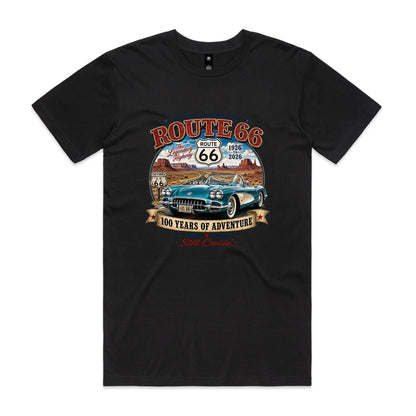 A black graphic t-shirt featuring a vintage-style Route 66 design. The print shows a teal classic Corvette car, desert canyons, and retro Route 66 signs with text reading 'ROUTE 66', 'The Legendary Highway', '1926 to 2026', '100 YEARS OF ADVENTURE', and 'Still Cruisin''.