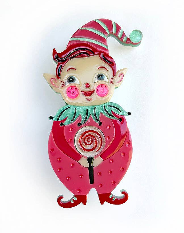 A whimsical enamel pin shaped like a strawberry with a small elf character on top, holding a lollipop. The pin features a vibrant pink strawberry body with red seeds, a green collar, and a red-and-green striped hat, set against a plain white background.
