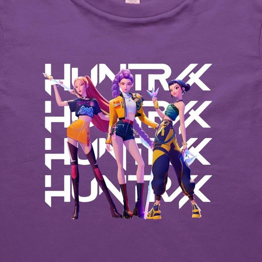 A close-up of a purple t-shirt featuring a graphic print of three stylized female anime characters in colorful outfits, overlaid with the word 'HUNTRX' repeated vertically in large white letters.