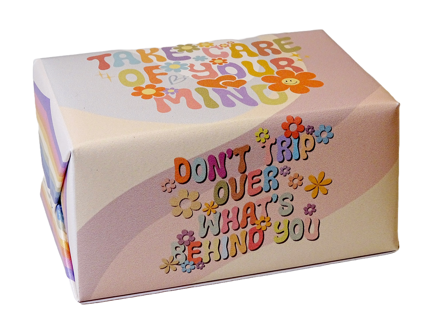 A square gift box with rounded corners featuring retro-style colorful text that reads 'TAKE CARE OF YOUR MIND' and 'DON'T TRIP OVER WHAT'S BEHIND YOU' decorated with small flower illustrations, shown on a plain white background.