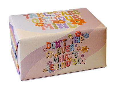 A square gift box with rounded corners featuring retro-style colorful text that reads 'TAKE CARE OF YOUR MIND' and 'DON'T TRIP OVER WHAT'S BEHIND YOU' decorated with small flower illustrations, shown on a plain white background.