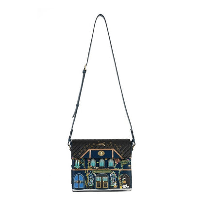 A black quilted crossbody handbag featuring a detailed, colorful illustration of a house facade on the front flap, complete with blue doors, green foliage, and gold accents, set against a plain white background.