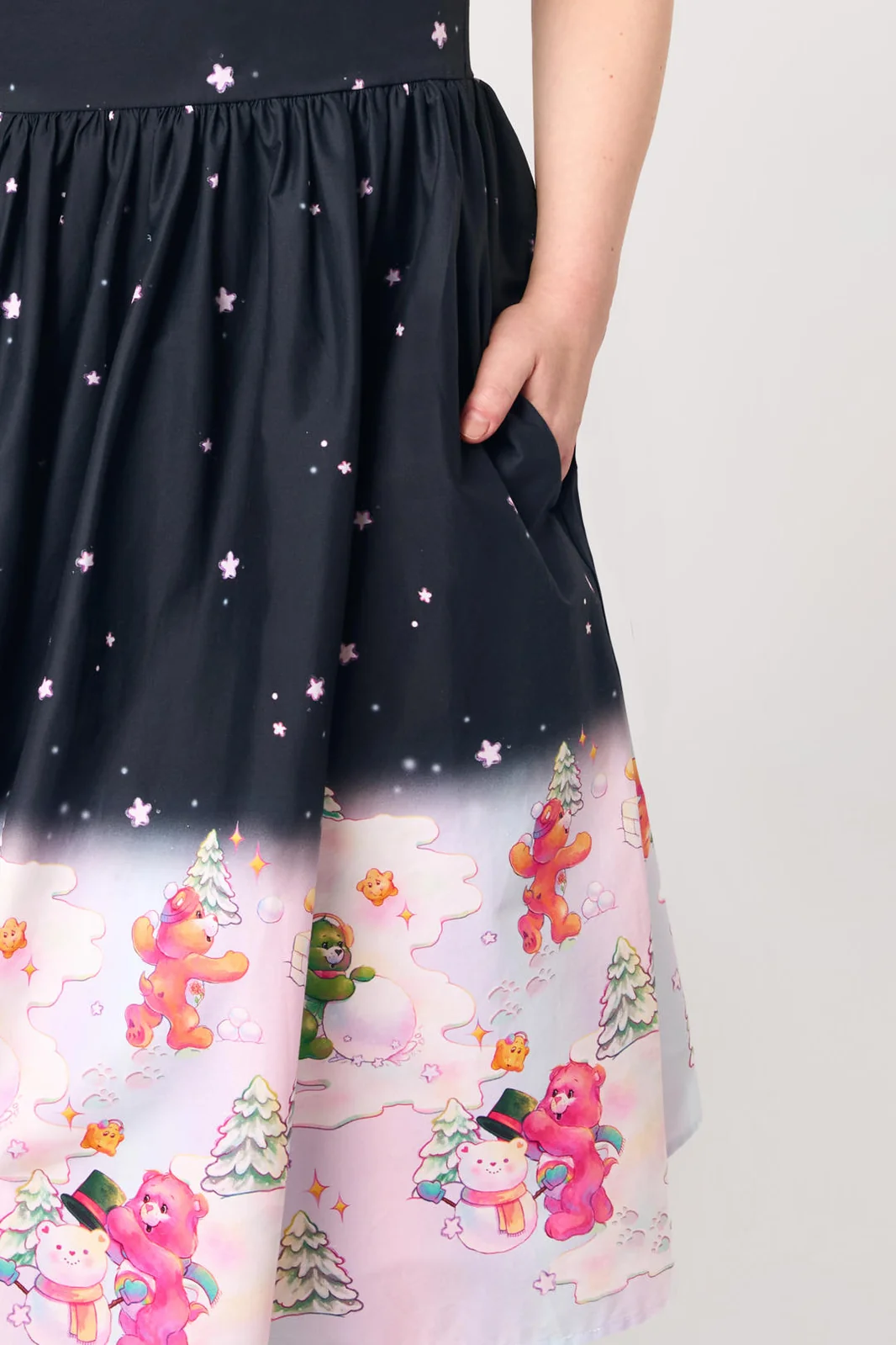 A close-up of a black midi skirt with a pink ombre gradient and a cartoon bear winter scene print at the bottom, featuring a side pocket with a hand in it.